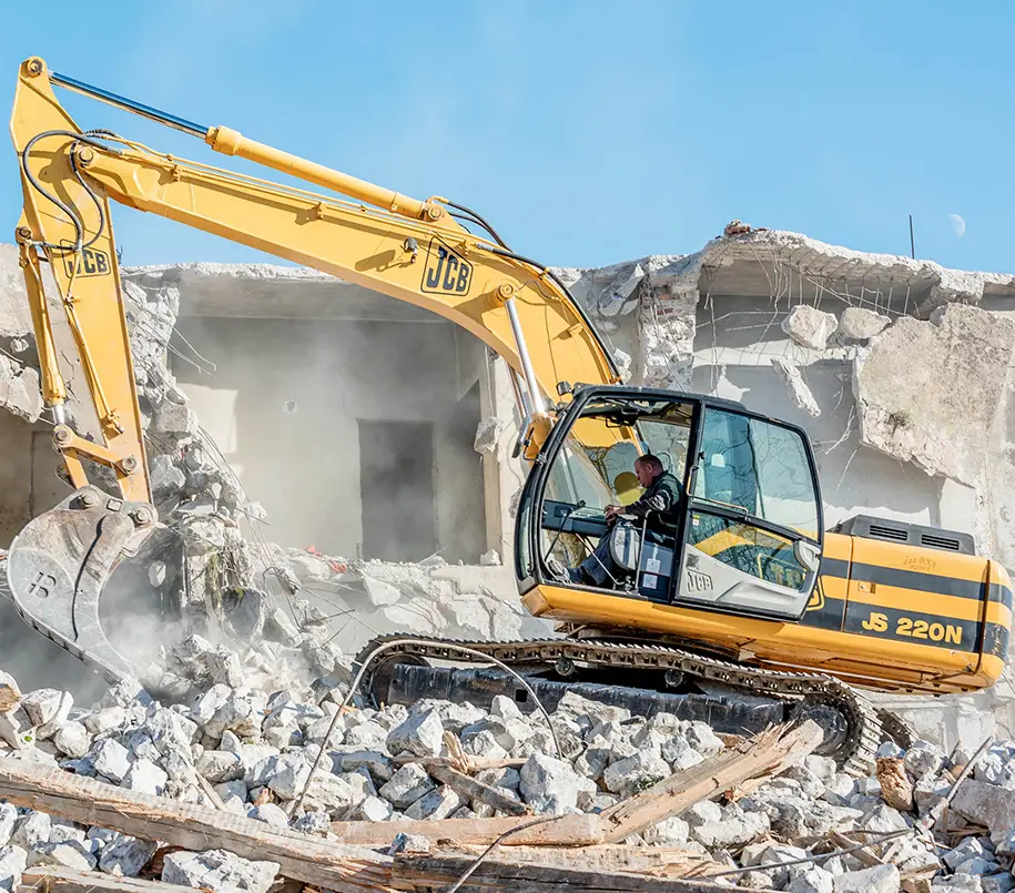 Bagger vor Gebäude zum Abbruch. Abbruchunternehmen sind meist in größere Projekte involviert, wie der Abbruch von Industriebauten, Brücken, Hochhäusern oder Infrastrukturen. Hier kann es auch um die Teilzerlegung von Gebäuden gehen, wenn bestimmte Teile erhalten oder Materialien wiederverwertet werden sollen.