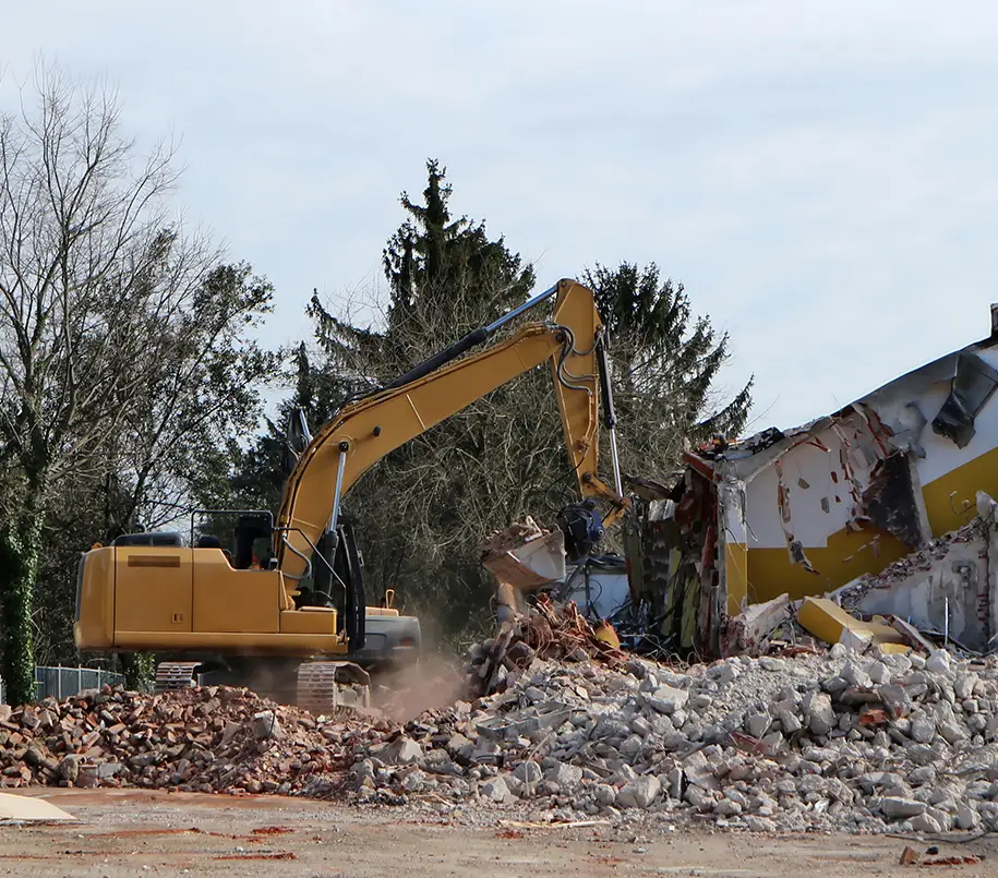 Bagger beim Abriss eines Hauses. Aushub von Fundamenten: Nach dem Abriss eines Gebäudes müssen oft auch die Fundamente und Kellerstrukturen entfernt werden. Bagger sind dabei essenziell, um den Erdaushub durchzuführen und die Fundamente freizulegen und zu entfernen.