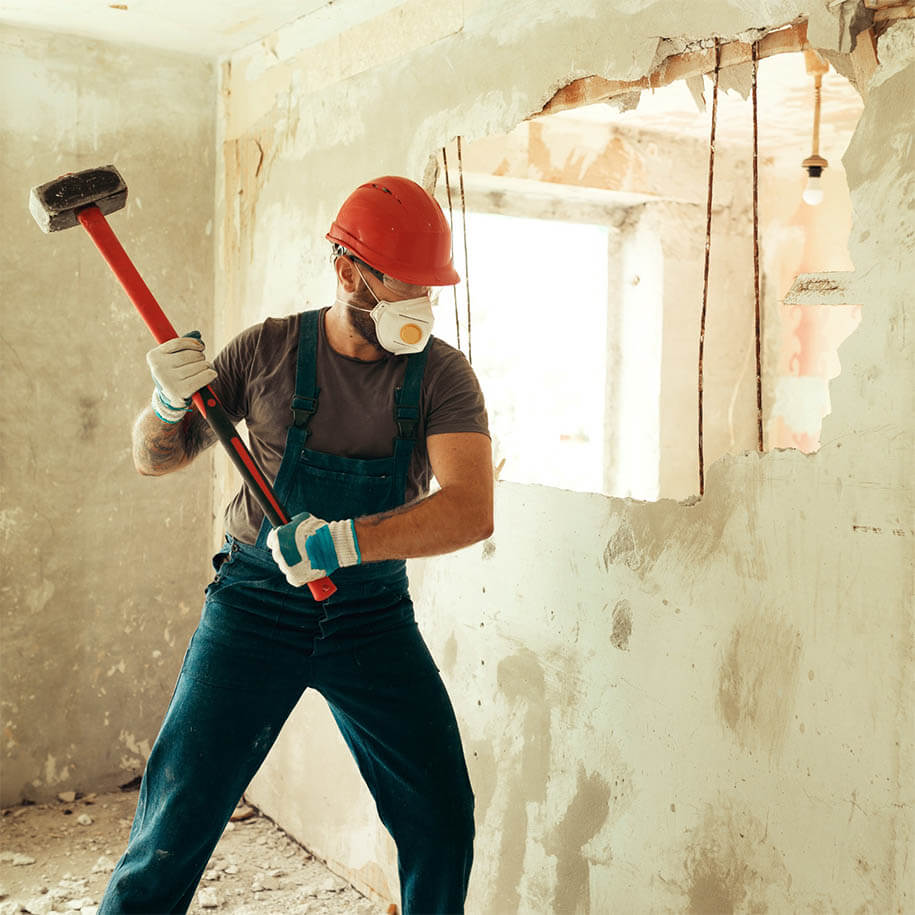 Arbeiter mit Helm und Schutzmaske beim Abriss einer Trockenbauwand