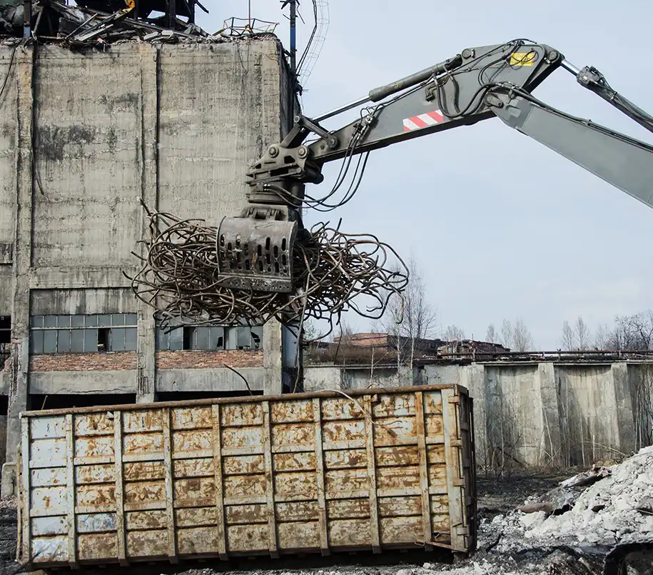 Bagger packt Material zum Recyceln in einen Container beim Abbruch von Lagerhallen